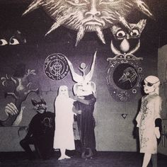 two women dressed in costumes standing next to each other with masks on the wall behind them