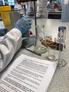 a lab worker in white coat and blue gloves holding a beakle filled with liquid