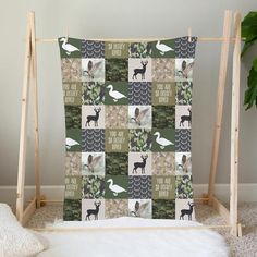 a green and white quilt with animals on it in front of a wooden frame next to a potted plant