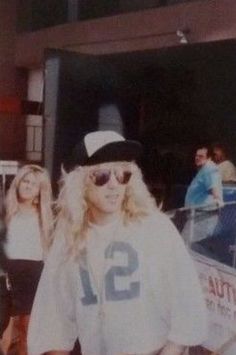 a woman in white shirt and black hat walking down street with other people behind her