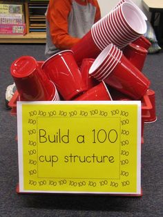 a pile of red cups sitting on top of a table next to a sign that says build a 100 cup structure