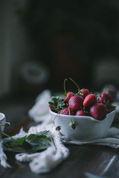 a white bowl filled with strawberries on top of a wooden table