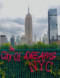 the city of dreams sign is covered in graffiti on a green fence with skyscrapers in the background