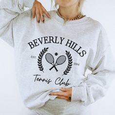 ✨Elevate your tennis game with our Beverly Hills Tennis Club Sweatshirt - a perfect blend of preppy style and California chic. This sweatshirt isn't just sportswear; it's a fashion statement that captures the essence of Beverly Hills' elegant tennis scene. 🎾 Immerse yourself in the sophisticated tennis culture of Beverly Hills with this stylish sweatshirt. The design embodies the charm and opulence of the renowned Beverly Hills tennis lifestyle. Our Beverly Hills Preppy Tennis Sweatshirt offers the perfect combination of style and comfort. Crafted from high-quality materials, it provides warmth on cooler days while maintaining a preppy, athletic look. ✿ PRODUCT SIZING ✿ ❃ Size charts are located within listing images - please consult size chart by style.  ❃ Most shirts fit true to size wi Athletic Club Sweatshirt, Sporty Tennis Sweatshirt With Graphic Print, Tennis Crewneck, Tennis Club Sweatshirt, Tennis Lifestyle, Vintage Phone Case, Tennis Shirts, Athletic Looks, Tennis Clubs