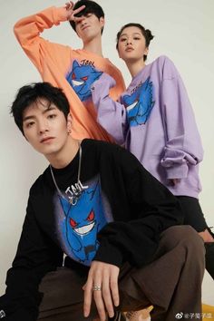 two young men sitting next to each other in front of a white wall wearing matching sweatshirts