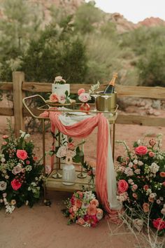 a table with flowers and a wine bottle on it in the middle of some bushes