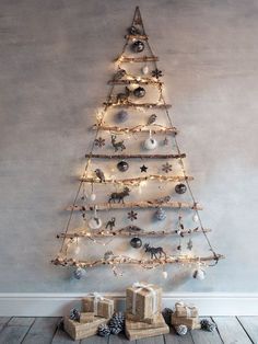 a small christmas tree with lights and presents under it on the floor in front of a wall