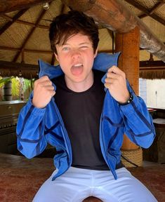 a young man sitting on top of a wooden bench holding his jacket over his shoulders