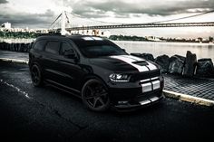 a black car parked in front of a body of water with a bridge in the background