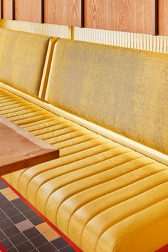 a long yellow bench sitting in the middle of a room with wood paneling on the walls