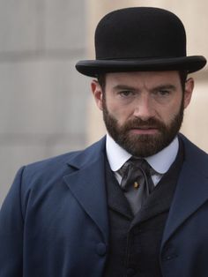 a man with a beard wearing a top hat and suit in front of a building