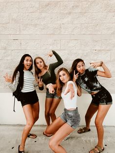 four girls posing for the camera in front of a brick wall with their fingers up