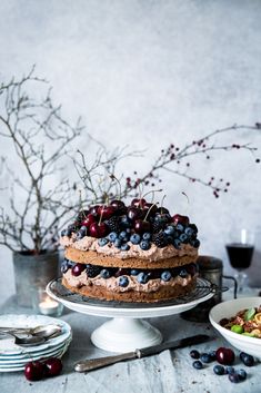 a cake with blueberries and blackberries on top sitting on a table next to plates