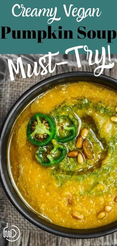 creamy vegan pumpkin soup in a black bowl with green peppers and pine nuts on top