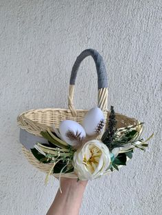 a hand holding a basket with flowers and eggs in it