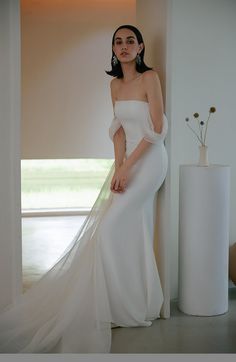 a woman in a white dress standing next to a vase