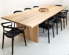 a wooden table surrounded by black chairs in a white room with a bowl on it