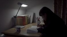 a person sitting at a desk in front of a lamp with books and pens on it