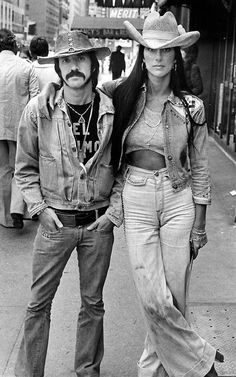 two people standing next to each other wearing cowboy hats and denim jackets, one man has his arm around the woman's shoulder