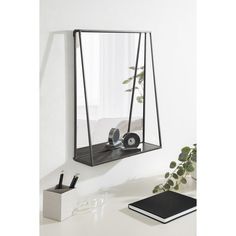 a mirror hanging on the side of a wall next to a desk with a plant