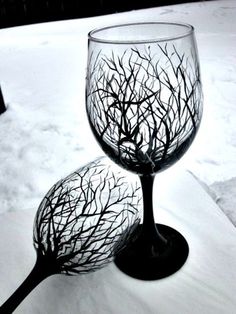 two wine glasses sitting in the snow with trees on them, one is empty and the other has no leaves