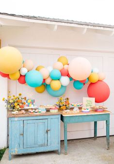 a table topped with lots of balloons next to a blue cabinet filled with cakes and cupcakes