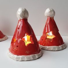 three red and white ceramic christmas hats with gold stars on the top one has a candle in it