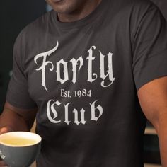 a man is holding a cup and smiling at the camera while wearing a t - shirt that says forty club