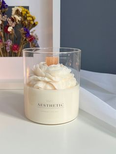 a glass jar filled with whipped cream on top of a white table next to flowers