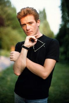 a man with red hair wearing a black shirt and holding his hand to his chin