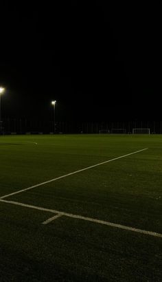 an empty soccer field at night with lights on the sidelines and grass in the foreground