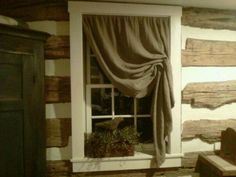 a window in a log cabin with curtains on the windowsill and potted plants next to it