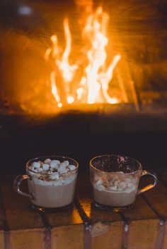 two mugs filled with hot chocolate sitting in front of a fire