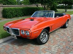 an orange muscle car parked in front of a house