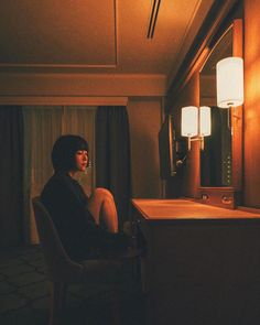 a woman sitting in a chair next to a desk with a lamp on top of it