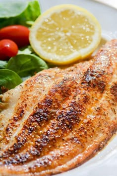 a white plate topped with fish next to a salad and lemon wedge on top of lettuce