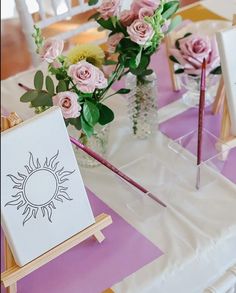 pink roses in vases are sitting on a table with easel and pencils