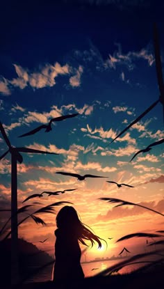 a girl standing in front of wind mills at sunset