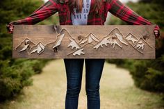 a woman holding a wooden sign with mountains on it