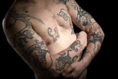 a man with tattoos on his arms and chest is posing for the camera in front of a black background