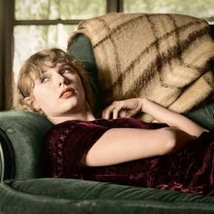 a woman laying on top of a green couch next to a brown blanket and window