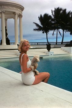 a woman sitting on the edge of a pool holding a dog