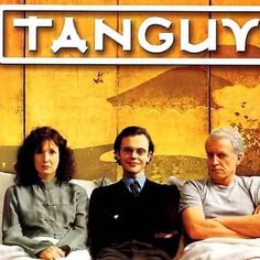 two men and a woman sitting on a couch in front of a sign that says tan guy