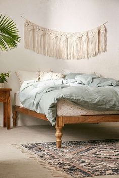 a rustic mango wood bed in a bedroom with fringes hanging on the wall above it