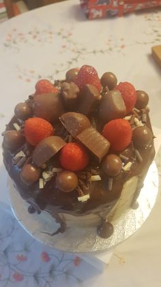 a chocolate cake with strawberries and nuts on top sits on a tablecloth covered table