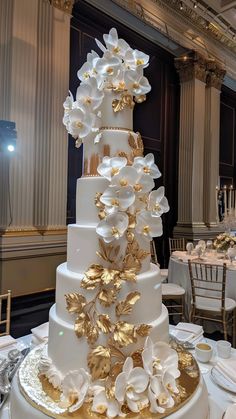 a large white and gold wedding cake with flowers on it's tiers in a banquet room