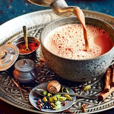 a person pouring tea into a cup on top of a metal tray with spices and cinnamons