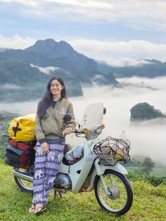 a woman sitting on top of a motorcycle next to a basket filled with luggage in the mountains