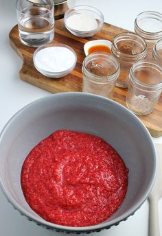 a bowl filled with red sauce on top of a wooden cutting board next to other ingredients