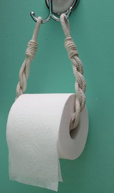 a roll of toilet paper hanging from a metal hook on a green wall with rope